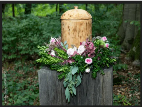 Urne funéraire écologique en bois entourée d'une couronne de fleurs fraîches en pleine forêt