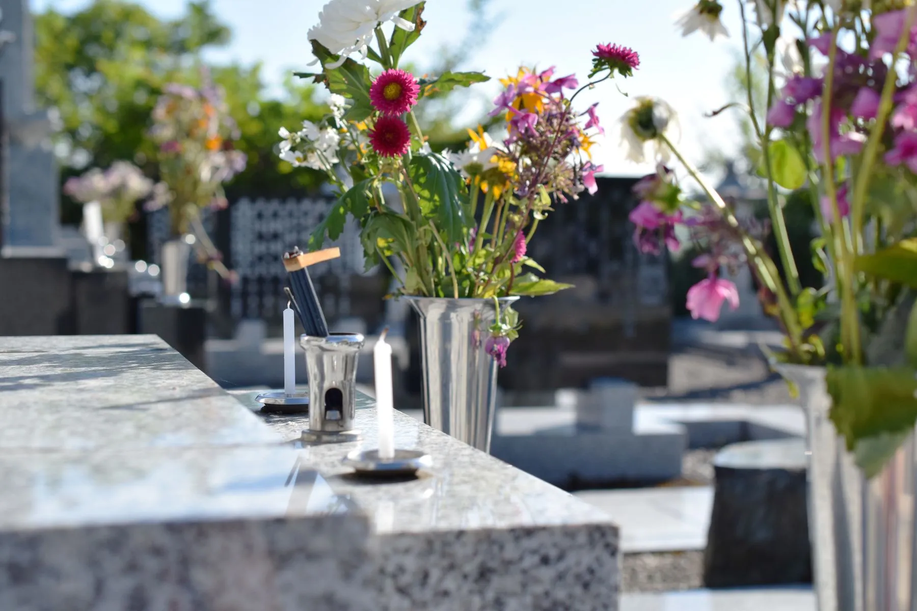 ase de fleurs et petites bougies posés sur une pierre tombale en granit rénovée